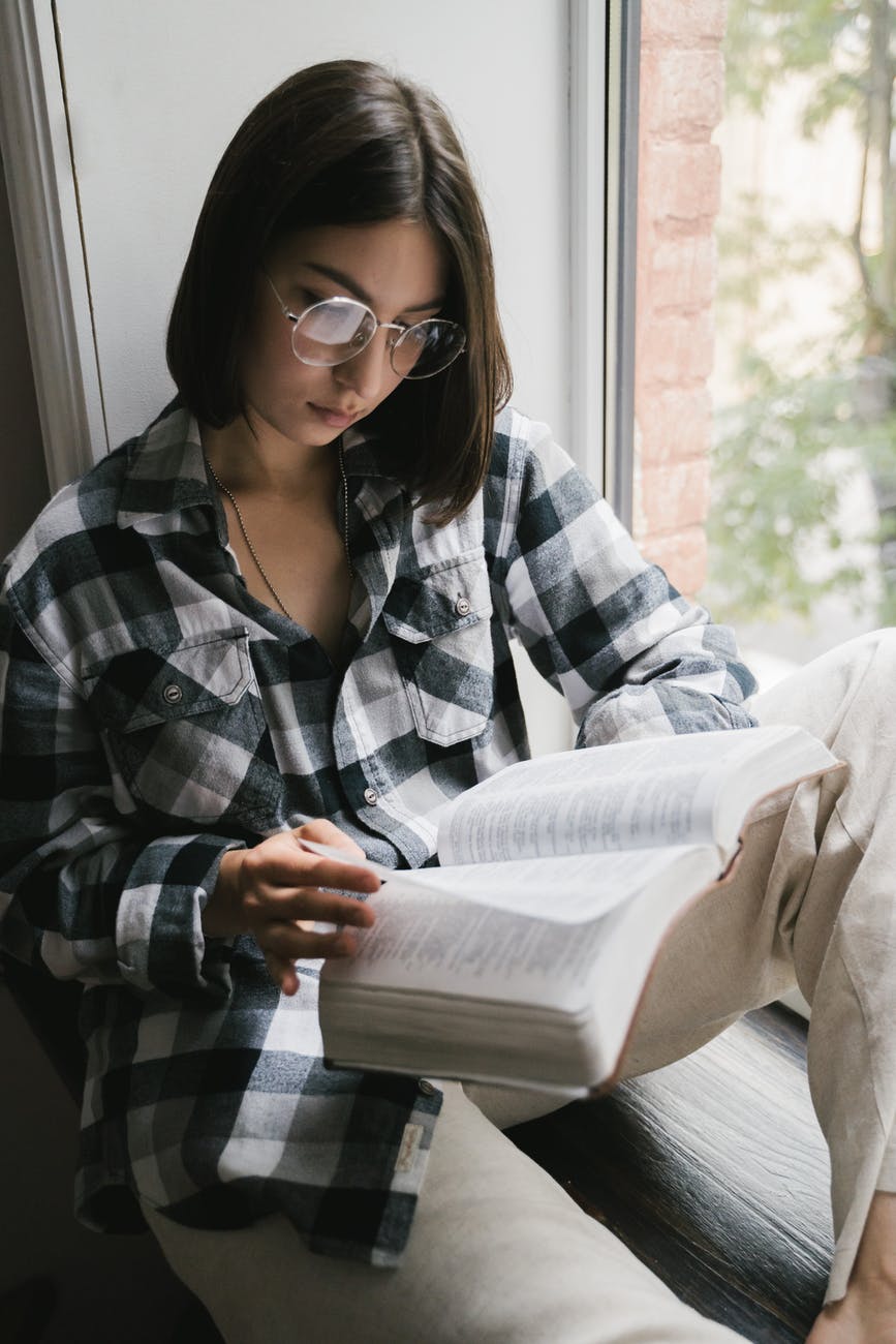 woman in black and white plaid dress shirt wearing black framed eyeglasses reading book